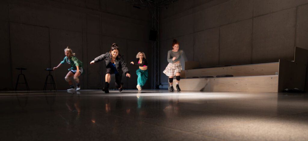 Vier Performerinnen rennen los. Sie bewegen sich auf einem Steinboden in einer großen Halle. Die Halle ist die Theaterhalle am Dom. Es ist eine Szene aus seven lives - none left