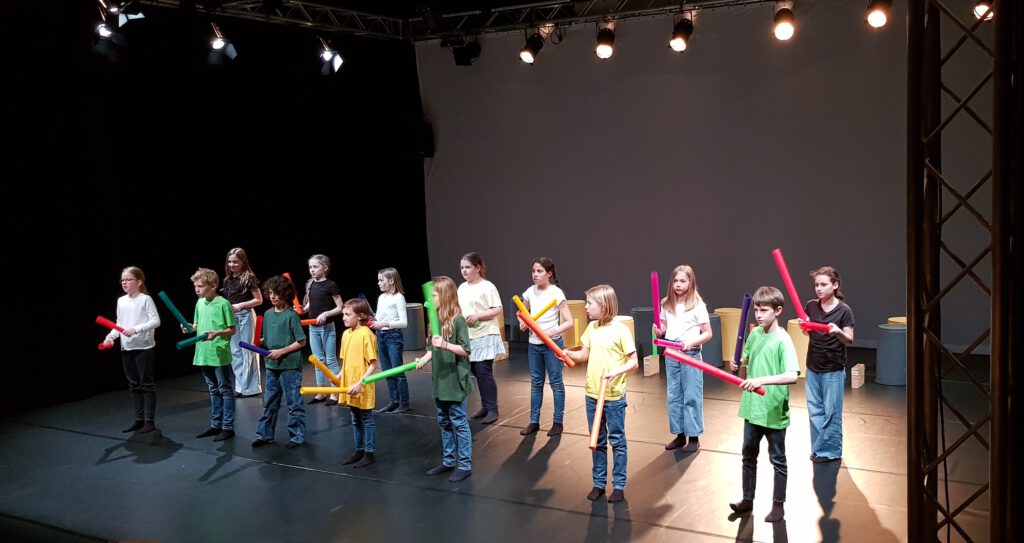Mitglieder des Vinzentinum Würzburg steht auf der Bühne der Theaterhalle am Dom. Sie haben bunte T-Shirts an. Sie halten bunte Kunststoffröhren in den Händen, mit denen sie musizieren.